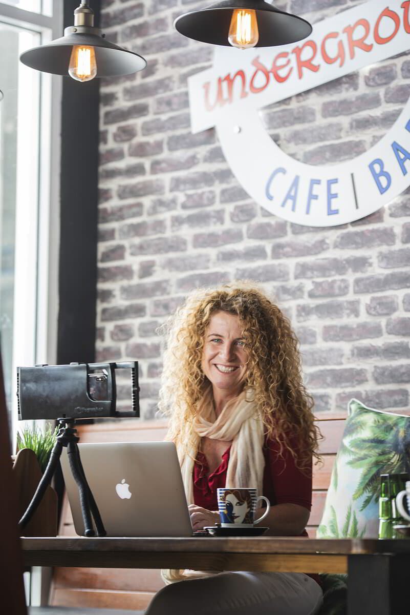 Lisa Monks smiling behind her laptop in a café, ready to record a training session