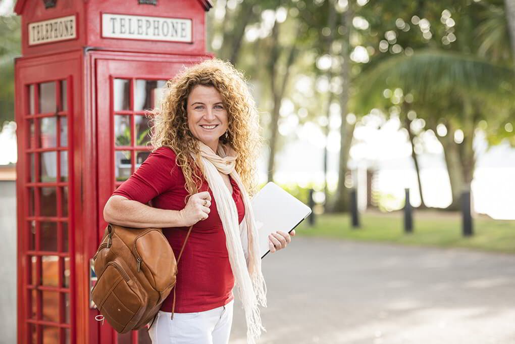 Lisa Monks with her laptop and leather backpack standing beside a red telephone box