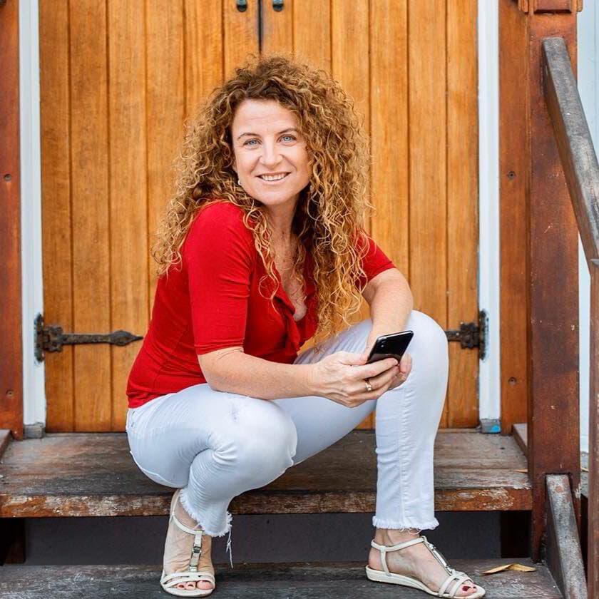 Lisa Monks sitting on timber steps with her phone, relaxed and smiling