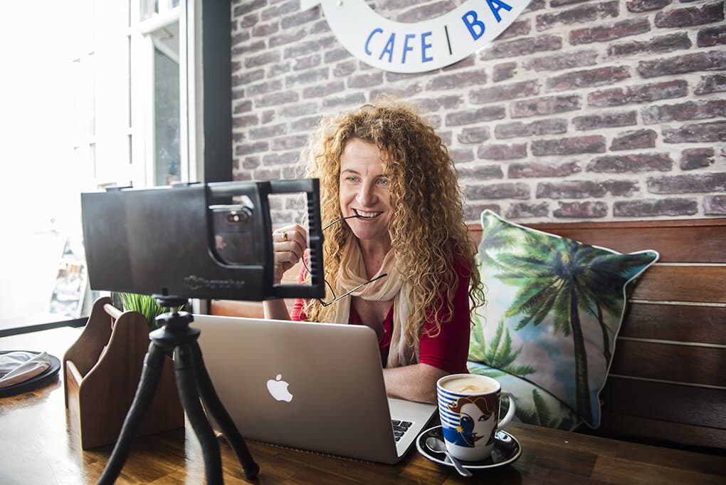Lisa Monks at a café table with her laptop and phone filming rig, planning content